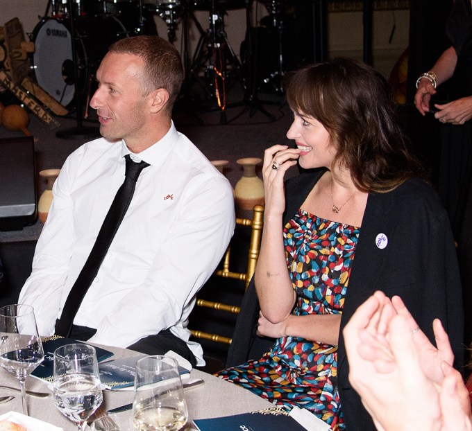 Chris Martin and Dakota Johnson look to the side and smile