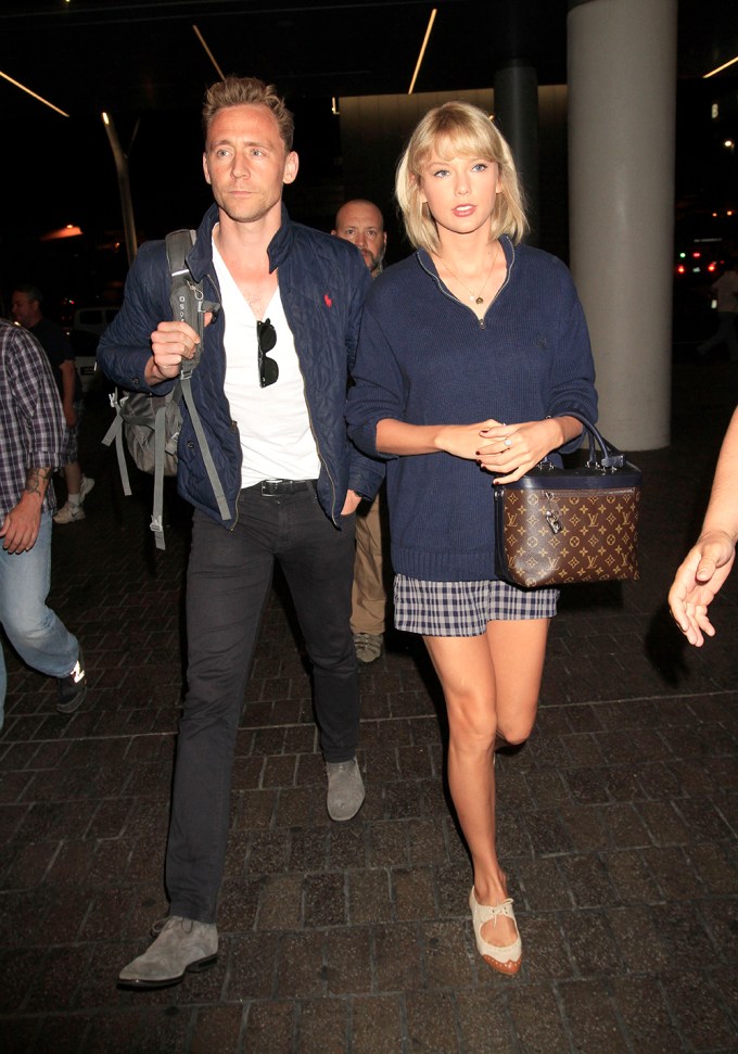Taylor Swift & Tom Hiddleston continue their world tour as they fly out of Los Angeles surrounded by several bodyguards. The “1989” singer & “The Avengers” actor were seen side by side as they caught a flight out of LAX.