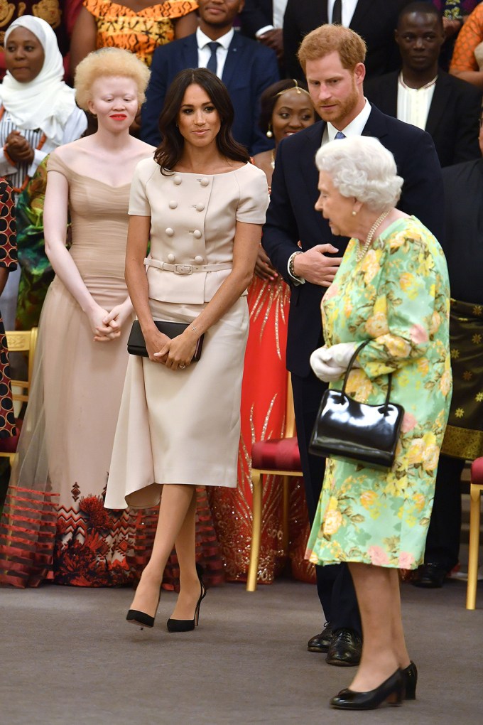 Meghan Markle & Prince Harry stand next to the Queen