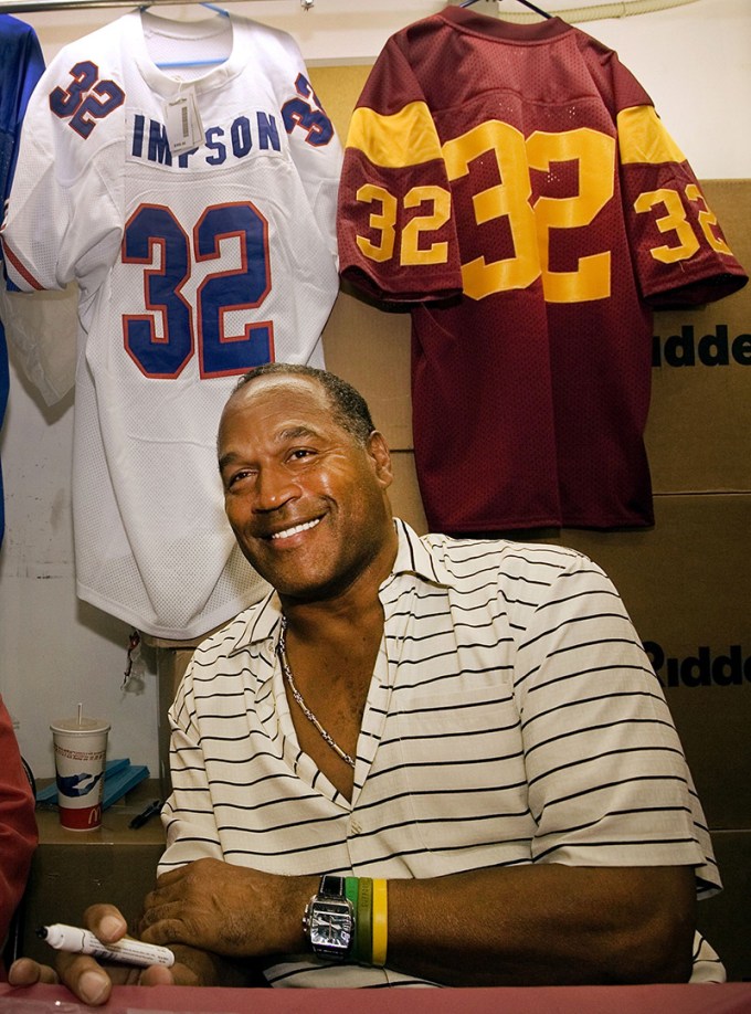 OJ Simpson smiles while posing in front of his football jerseys