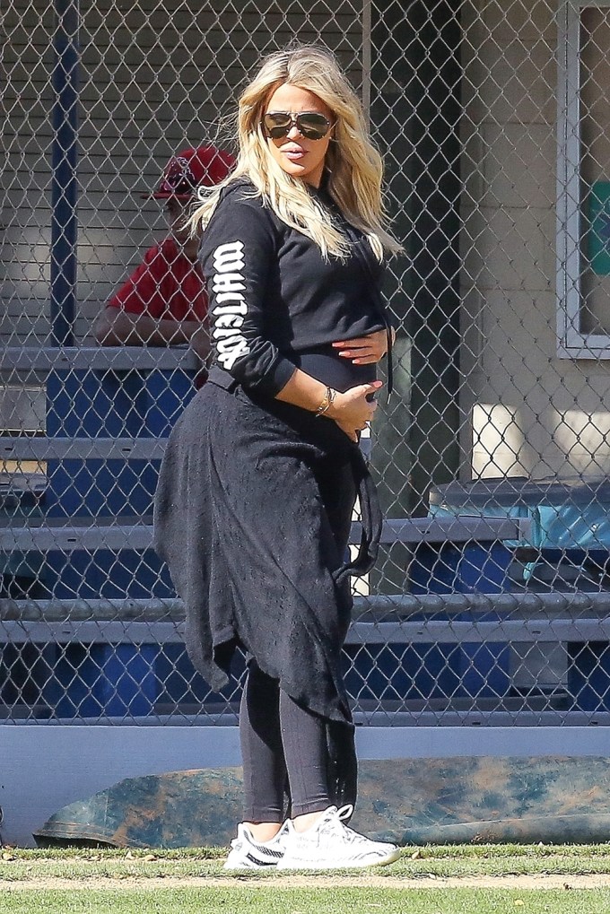 Khloe Kardashian caresses her baby bump on the Baseball Diamond