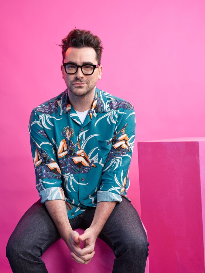 Dan Levy poses while in front of a pink background