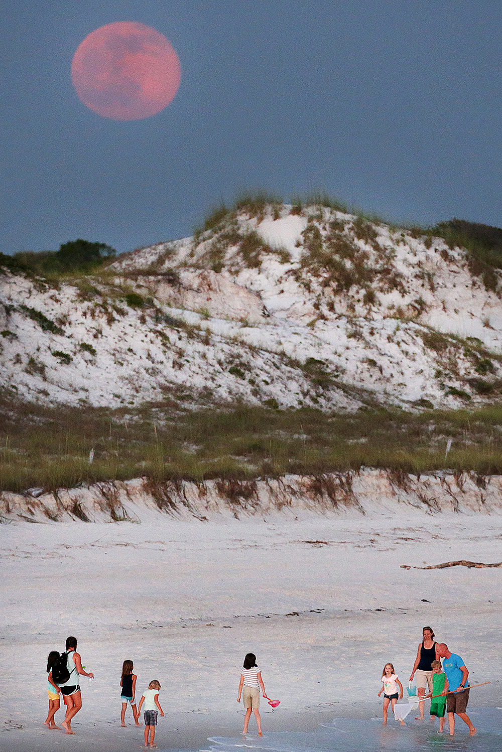 In this photo taken Monday, June 20, 2016, beachgoers enjoy the final moments of daylight as the strawberry moon rises behind them at St. Andrews State Park in Panama City Beach, Fla.  (Patti Blake/News Herald via AP) MANDATORY CREDIT