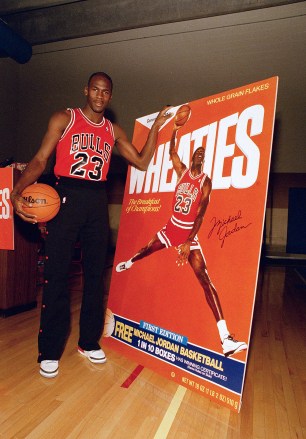 Michael Jordan dari Chicago Bulls berpose di samping patungnya di atas sekotak Wheaties selama upacara pembukaan di Chicago, .  Jordan adalah atlet selebritas ketujuh yang menampilkan gambarnya di kotak sereal yang dipasarkan sebagai "Sarapan Sang Juara Bulls Jordan Wheaties 1988, Chicago, AS