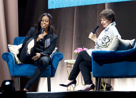 Former first lady Michelle Obama, left, gestures at her aching feet in high heels as she is accompanied by former Senior Advisor to President Barack Obama, Valerie Jarrett, right, speaking to the audience as she presents her anticipated memoir "Becoming" during her book tour stop in Washington, Saturday, Nov. 17, 2018. (AP Photo/Jose Luis Magana)
