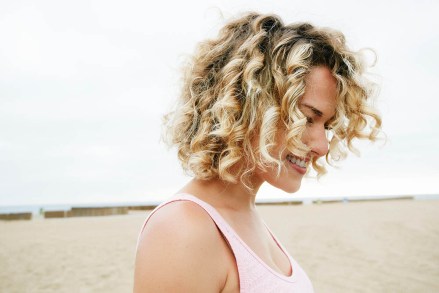 MODEL RELEASED Portrait of smiling young woman with blond curly hair standing on sandy beach.
VARIOUS