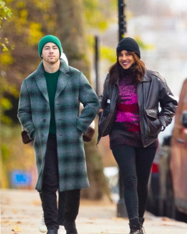 EXCLUSIVE: Nick Jonas and wife Priyanka Chopra Jonas go sightseeing around London ahead of the Christmas holidays. The couple, who have been married for two years, wore face masks and stopped for a hot drink at a cafe. The Bollywood actress who is in town to film 'Text for You', looked positively glowing. The happy couple could be seen stopping for Nick to take some funny photos of Priyanka next to a Highway Maintenance van, presumably to have the words ‘High Maintenance’ behind her. The loved up pair could be seen walking along with Priyanka’s mother in tow, always a couple of yards behind them. Nick, 28, and Priyanka, 38, could be seen wearing Christmas colors, with Nick in a green beanie hat and green accented checked woolen overcoat, while Priyanka opted for a dark brown leather jacket with red and pink knitted top, beanie hat, and jeans. 09 Dec 2020 Pictured: Nick Jonas, Priyanka Chopra Jonas. Photo credit: MEGA TheMegaAgency.com +1 888 505 6342 (Mega Agency TagID: MEGA720310_003.jpg) [Photo via Mega Agency]