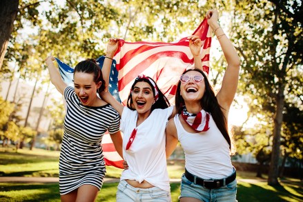 Cheerful female friends running around the park with American flag. Young and enthusiastic American girls enjoying 4th of july holiday at park.; Shutterstock ID 1377382046; Comments: art use