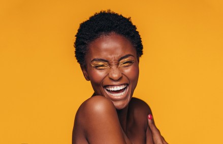 Cheerful young african woman with vivid makeup on her eyes. Female model laughing against yellow background.; Shutterstock ID 741676036; Comments: art use