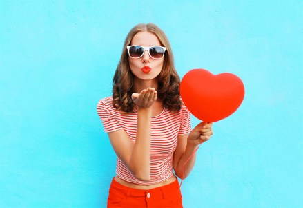 Portrait pretty woman sends air kiss with red balloon heart shape over blue background; Shutterstock ID 573140110; Comments: art use