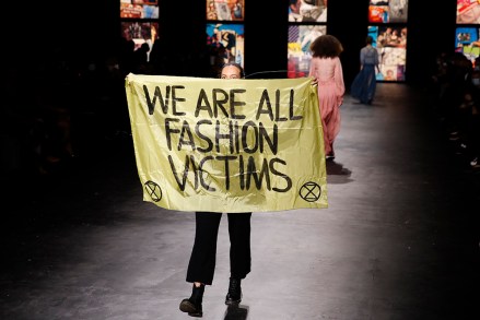 An activist displays a banner during Dior's Spring-Summer 2021 fashion collection presented Tuesday, Sept. 29, 2020 during the Paris fashion week. (AP Photo/Francois Mori)