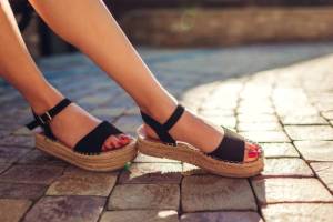 Stylish woman wearing black summer shoes with straw soles