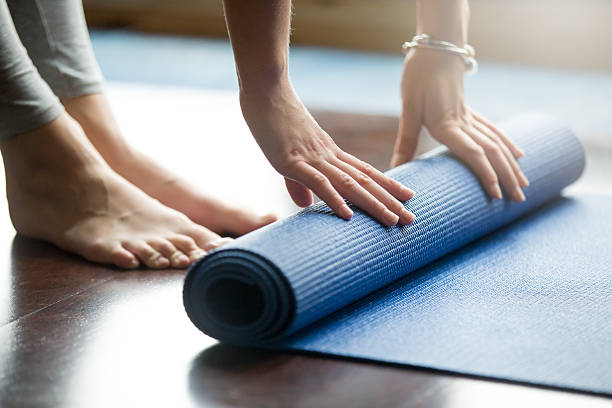 Close-up of a woman rolling up her blue yoga mat after working out at home.