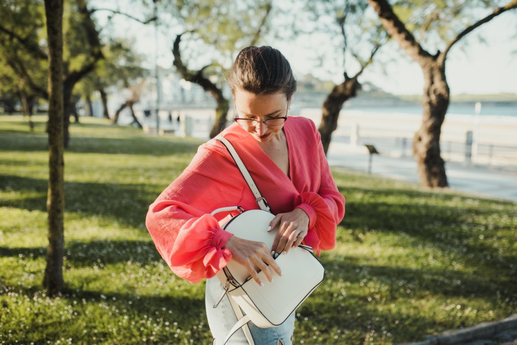 Young woman searching in her purse in a public park at sunset
