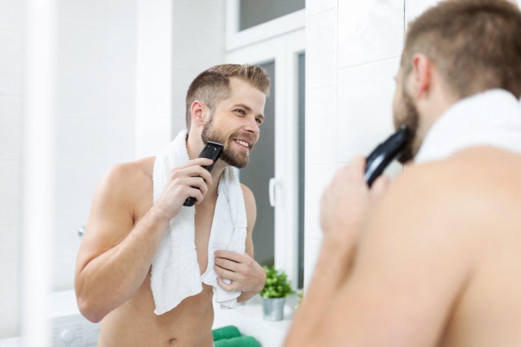 Bearded man trims his beard with an electric razor
