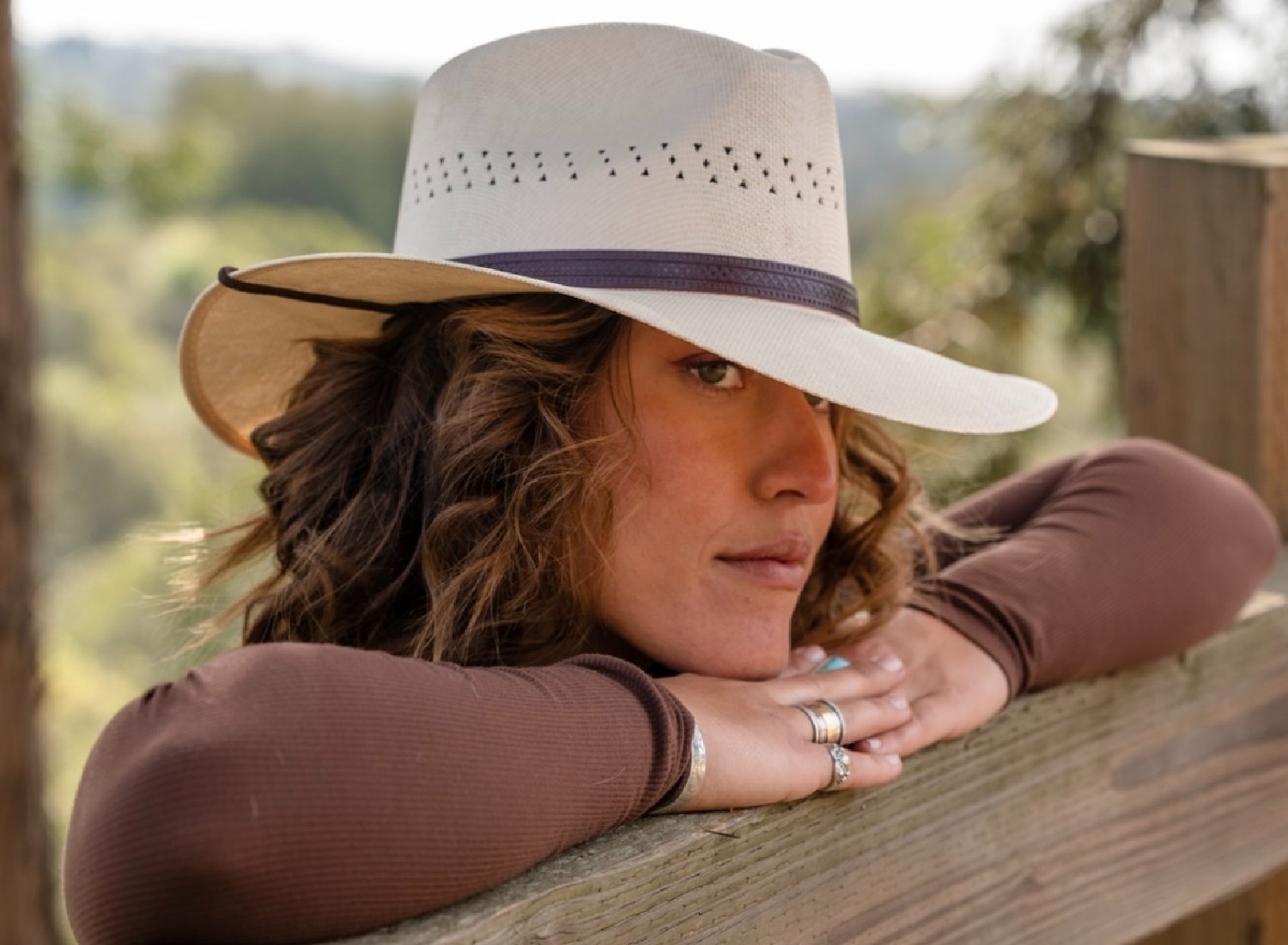 A woman leans on a fence wearing a straw hat