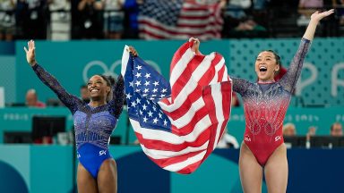 PARIS, FRANCE - AUGUST 1: Simone Biles of United States (L) and Sunisa Lee of United States (R) celebrate their victory and third place holding the USA flag during the Women's All-Around Final on day six of the Olympic Games Paris 2024 at Bercy Arena on August 1, 2024 in Paris, France. (Photo by Daniela Porcelli/Eurasia Sport Images/Getty Images)