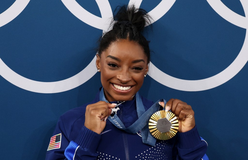 PARIS, FRANCE - AUGUST 01: (EDITOR'S NOTE: Alternate crop) Gold medalist Simone Biles of Team United States poses with the Olympic Rings and a goat charm on her necklace during the Artistic Gymnastics Women's All-Around Final medal ceremony on day six of the Olympic Games Paris 2024 at Bercy Arena on August 01, 2024 in Paris, France. (Photo by Jamie Squire/Getty Images)