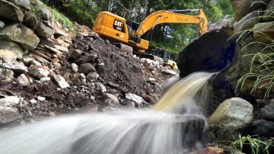 Zapora na stawie w Dudleyville została rozebrana przez ciężki sprzęt budowlany po wydaniu nakazu awaryjnego ze względu na wysokie ryzyko awarii. Podczas usuwania wody z przepustu znajdującego się w tamie wylewała się woda. (Zdjęcie: John Tlumacki/The Boston Globe za pośrednictwem Getty Images)