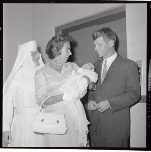 (Título original) La Sra. Ethel Kennedy, (izq.), sostiene durmiendo a Christopher George, de 8 días, su octavo hijo, mientras su esposo, Attny. El general Robert F. Kennedy observa cómo la pareja sale del Hospital St. Elizabeth. Condujeron hasta el Aeropuerto Internacional Logan, donde abordaron un avión con destino a Hyannis Port.