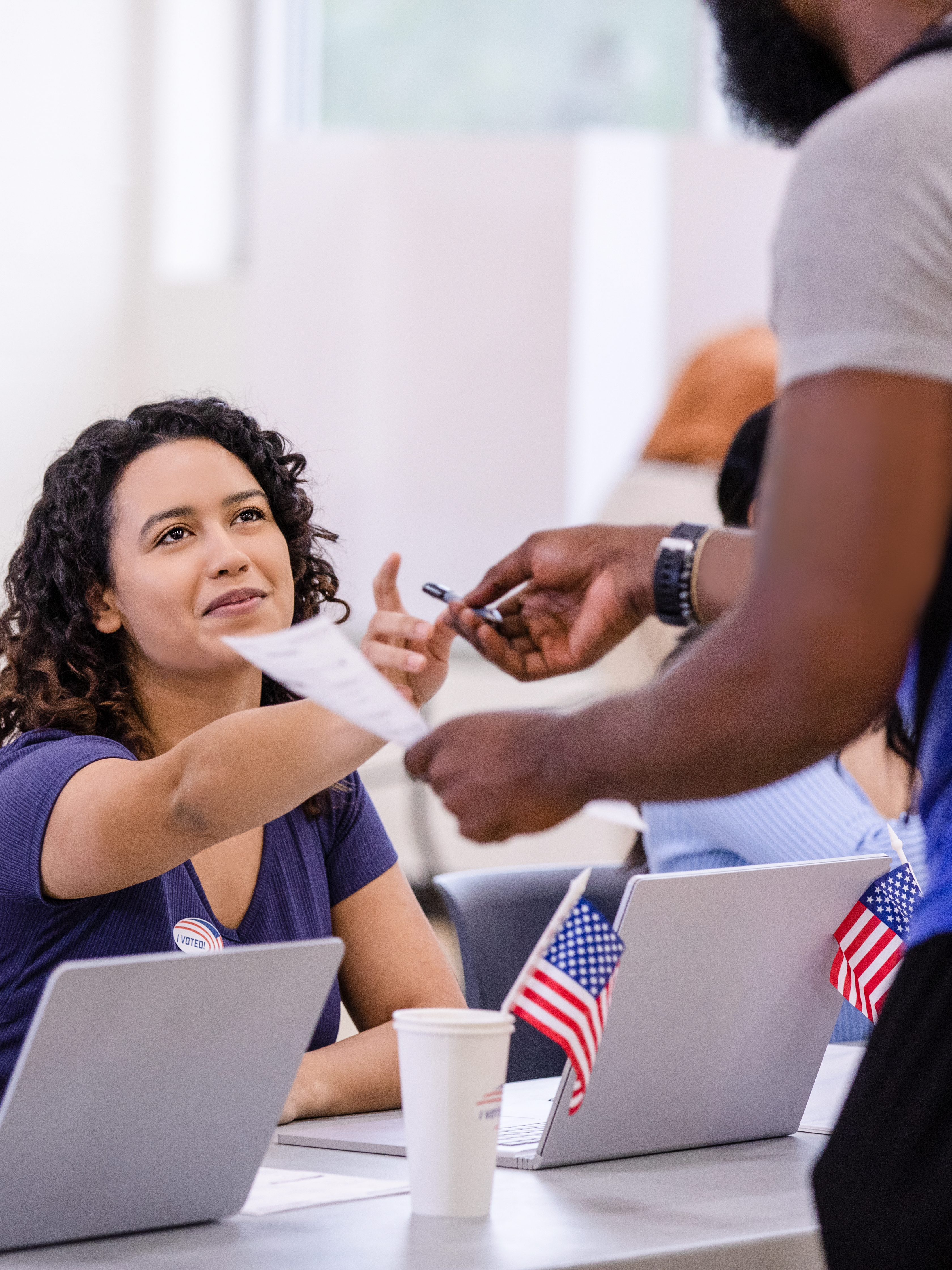 Two cheerful female volunteers help the unrecognizable young adult with his ballot for the election.