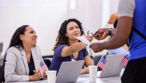 Two cheerful female volunteers help the unrecognizable young adult with his ballot for the election.