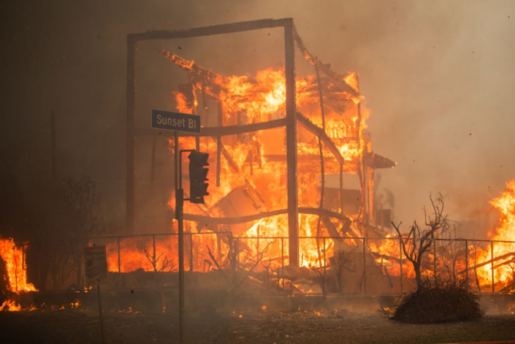 LOS ANGELES, CALIFORNIA - JANUARY 8: Flames from the Palisades Fire burn a building on Sunset Boulevard amid a powerful windstorm on January 8, 2025 in the Pacific Palisades neighborhood of Los Angeles, California. Fueled by intense Santa Ana Winds, the Palisades Fire has grown to over 15,000 acres and 30,000 people have been ordered to evacuate while a second major fire continues to burn near Eaton Canyon in Altadena.  (Photo by Apu Gomes/Getty Images)