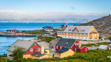 A fog bank covers the far shore and mountains as ice floes float past the colorful buildings and homes in Nuuk, Greenland