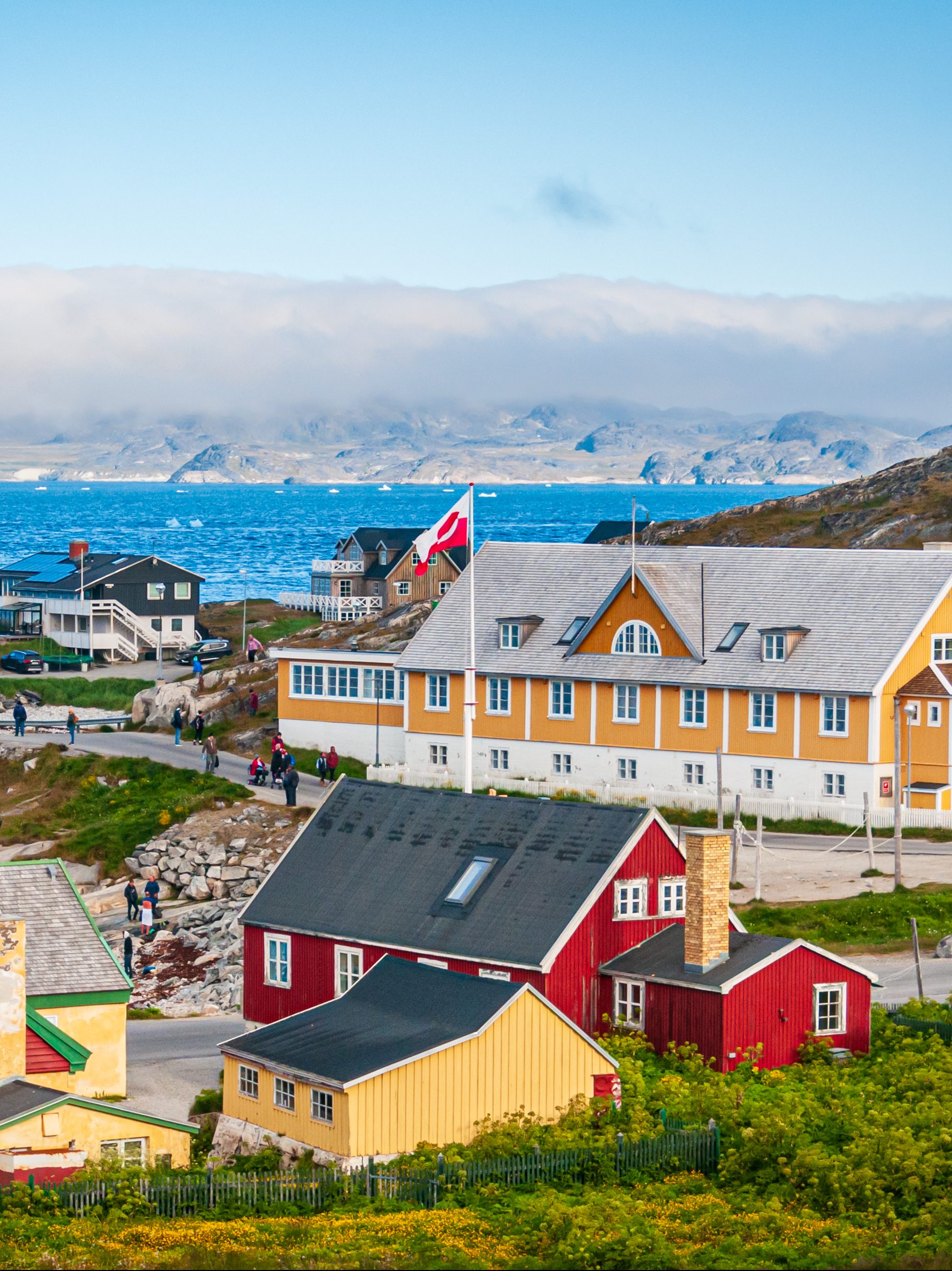 A fog bank covers the far shore and mountains as ice floes float past the colorful buildings and homes in Nuuk, Greenland