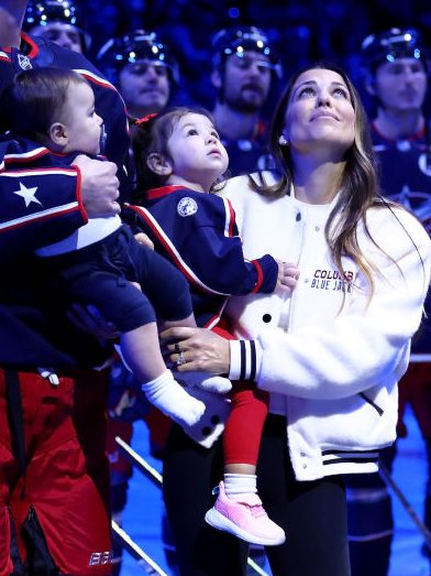 COLUMBUS, OHIO - OCTOBER 15:  Sean Monahan #23 of the Columbus Blue Jackets stands on the ice while holding former Columbus Blue Jackets player Johnny Gaudreaus son, Johnny Jr, along side Gaudreaus wife and daughter, Meredith and Noah, and his brother-in-law Eddie Morris, during a remembrance ceremony prior to the start of the game against the Florida Panthers at Nationwide Arena on October 15, 2024 in Columbus, Ohio. Gaudreau and his brother Matthew were killed when hit by a suspected drunk driver on August 29, 2024.(Photo by Kirk Irwin/NHLI via Getty Images)